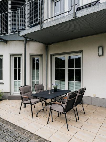 Eine gemütliche Terrasse mit einem schwarzen Tisch und sechs Stühlen. Der Bereich ist von Fenstern umgeben und hat eine moderne Atmosphäre.