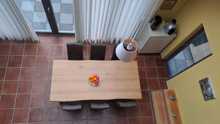 Ein moderner Essbereich mit einem großen Holztisch und Stühlen. Auf dem Tisch steht eine Obstschale. 