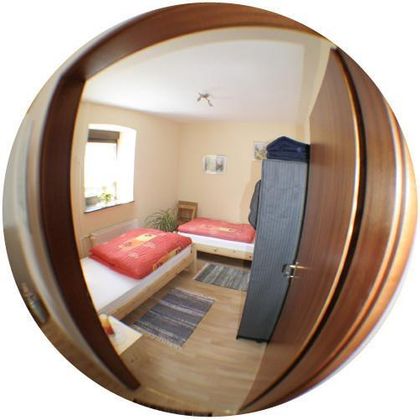 Ein einfaches Zimmer mit zwei Betten und einem kleinen Tisch. Die Wände sind hell, und es gibt ein Fenster, das natürliches Licht hereinlässt.