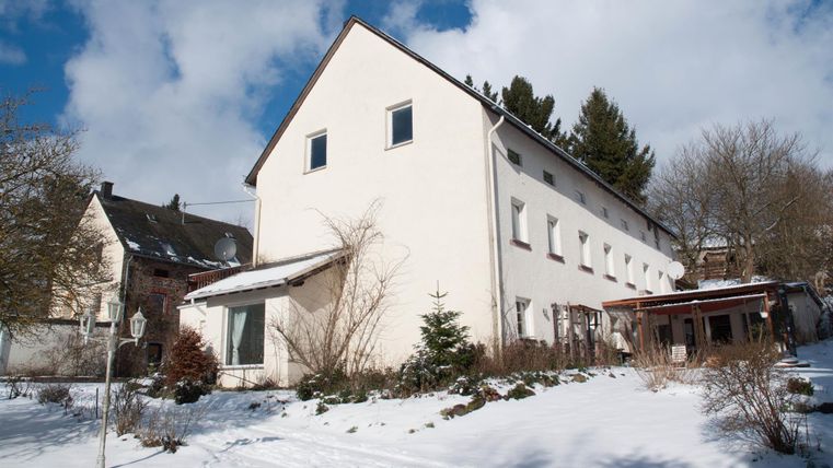 Ein modernes, weißes Gebäude im Schnee, umgeben von schneebedecktem Boden und winterlichen Bäumen. Der Himmel ist klar mit einigen Wolken.