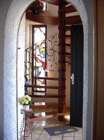 Ein schöner Eingangsbereich mit einer Holzspindeltreppe und buntem Glasfenster. Der Boden ist gefliest und es steht eine Blumenvase auf einem kleinen Tisch.