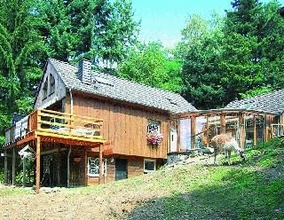 Ein charmantes Holzhaus inmitten von Bäumen. Im Vordergrund ist ein kleiner Garten mit einem Tier zu sehen.