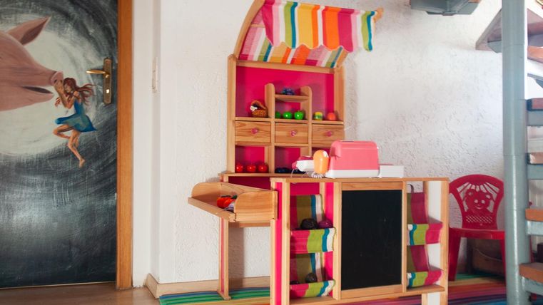 Ein buntes Spielküchen-Set steht in einem Raum. Es gibt eine hübsche Theke mit Lebensmittelspielzeug und farbigen Regalen.