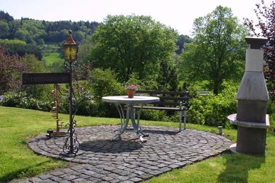 Ein schöner Garten mit einem runden Tisch und einer Bank. Grünes Gras und Bäume umgeben die Sitzecke.