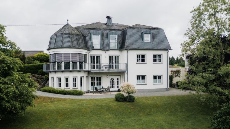 Ein schönes Haus mit mehreren Fenstern und einem einzigartigen Dach. Der Garten ist grün und gepflegt, ideal für entspannte Momente im Freien.