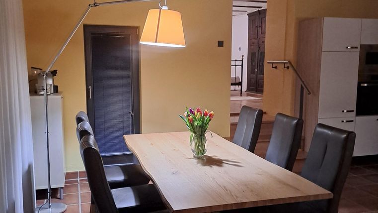 Ein einladender Essbereich mit einem großen Holztisch und sechs gemütlichen Stühlen. Eine Lampe hängt über dem Tisch, und ein Blumenstrauß steht in der Mitte.