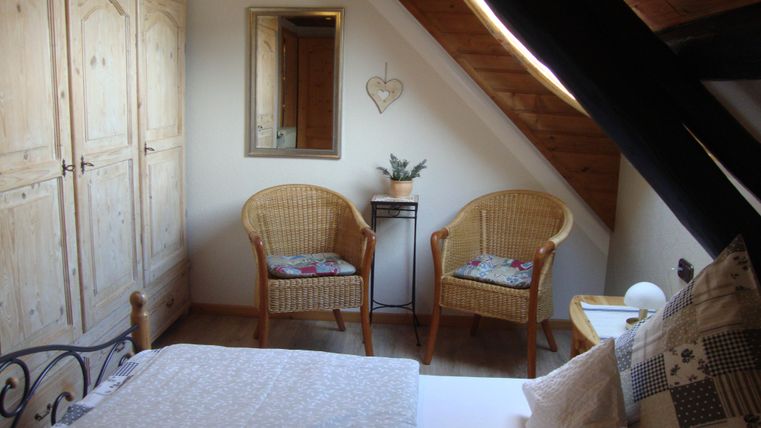 Ein gemütliches Schlafzimmer mit einem Bett und zwei Stühlen. Der Raum hat helle Wände und ein Holzinterieur.