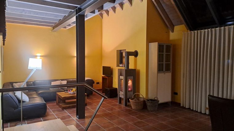 Ein gemütlicher Wohnraum mit einer dunklen Couch und einem Kamin. Die Wände sind gelb gestrichen, und es gibt große Fenster mit Vorhängen.
