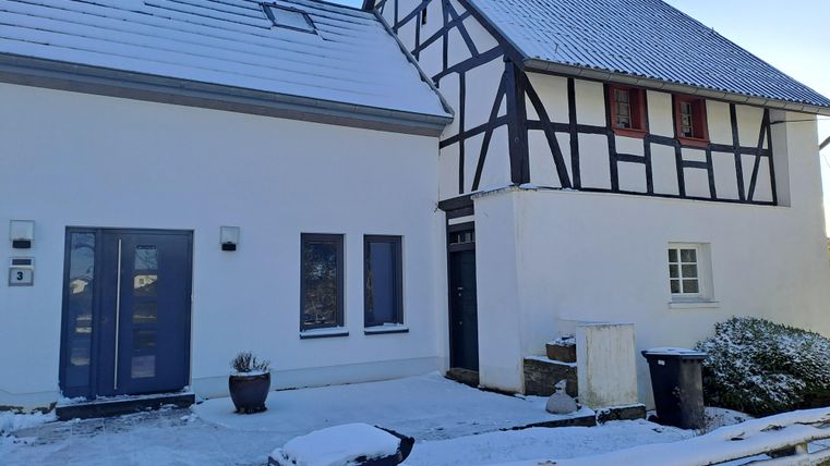 Ein charmantes Haus mit Fachwerk-Elementen und einem modernen Anbau. Der Boden ist mit Schnee bedeckt, und es ist ein klarer Himmel zu sehen.