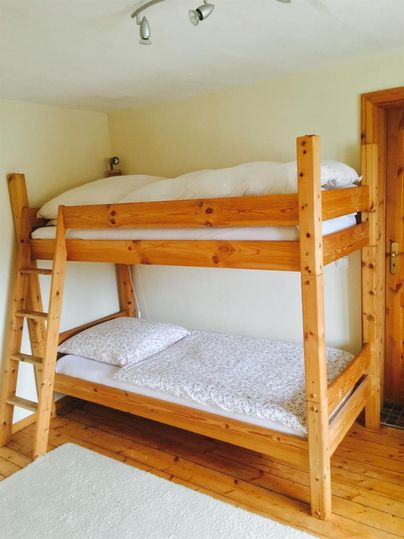Ein gemütliches Zimmer mit einem Etagenbett aus Holz. Es gibt frische Bettwäsche und einen warmen, einladenden Stil.