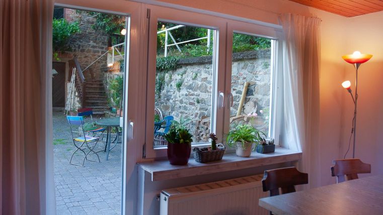 Ein Aufenthaltsraum mit Blick auf einen Garten. Draußen sind Stühle und Tische sowie eine Treppe im Hintergrund.