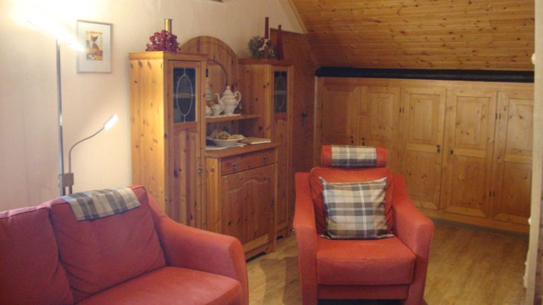 Ein gemütliches Wohnzimmer mit roten Sofas und Holzregalen. Die Wände sind hell, und der Boden ist aus Holz.