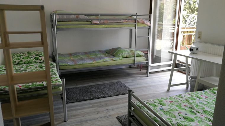 Ein einfaches Zimmer mit Hochbetten und Einzelbetten. Es gibt einen Tisch und einen offenen Zugang zum Balkon.