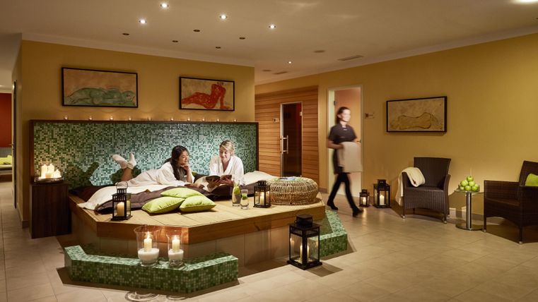 Ein entspannender Spa-Bereich mit einer komfortablen Liege und Kerzenlicht. Zwei Personen genießen eine Wellness-Auszeit in einer angenehmen Atmosphäre.