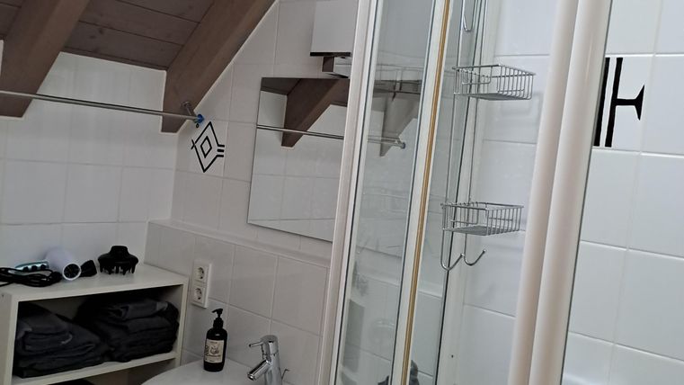 Ein modernes Badezimmer mit Dusche und Waschbecken. Die Wände sind hell gefliest und es gibt eine offene Regaleinheit für Handtücher.
