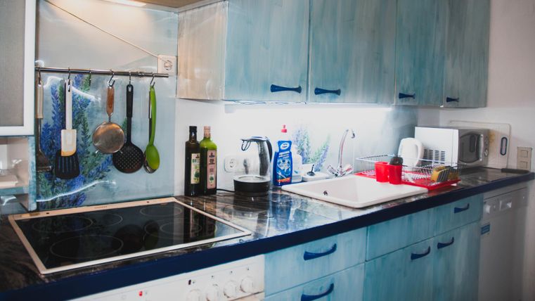 Eine moderne Küche mit blauen Schränken und einer Arbeitsplatte. Es sind Kochutensilien sowie Wasserkocher und Geschirr sichtbar.