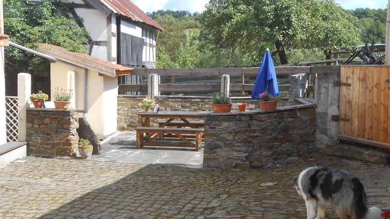 Ein schöner Innenhof mit natursteinerne Wänden und einem Holzplatz. Ein Hund spielt im Hintergrund und ein blauer Sonnenschirm steht auf dem Tisch.