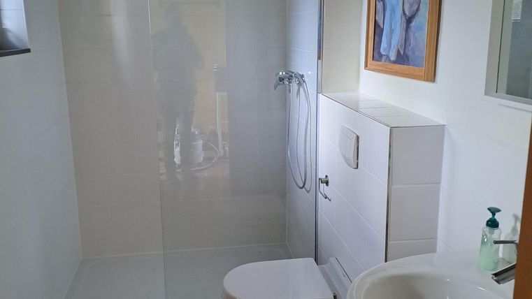 Ein modernes Badezimmer mit einer Glasdusche und einem Waschbecken. Die Wände sind hell und es gibt einen hochwertigen Bodenbelag.