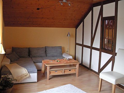 Ein gemütliches Wohnzimmer mit einem grauen Sofa, einem Holztisch und einem hellen Holzdecken. An der Wand sind moderne und traditionelle Elemente kombiniert.