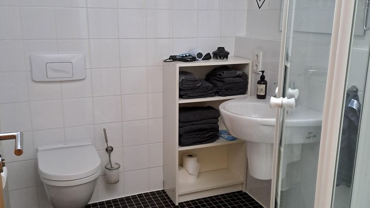 Ein modernes Badezimmer mit Dusche, Waschbecken und WC. Die Wände sind gefliest und es gibt einen schlichten Regal für Handtücher.