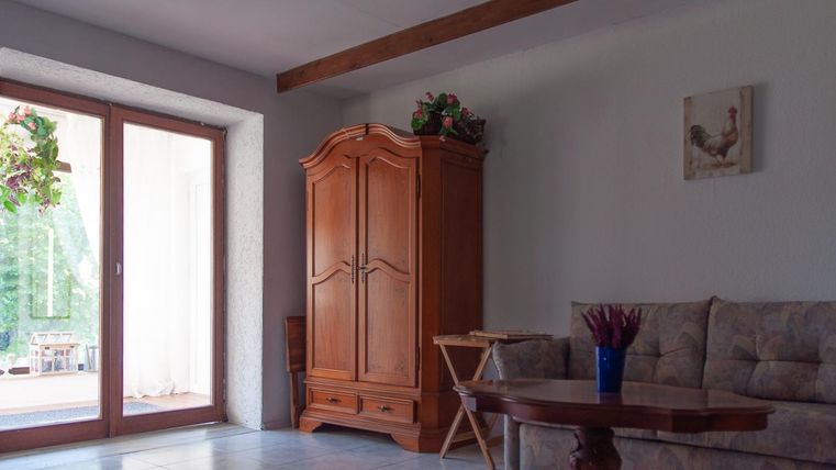 Ein gemütlicher Wohnraum mit einem beigen Sofa, einem Holztisch und einem großen Schrank. Durch das Fenster strömt Tageslicht in den Raum.