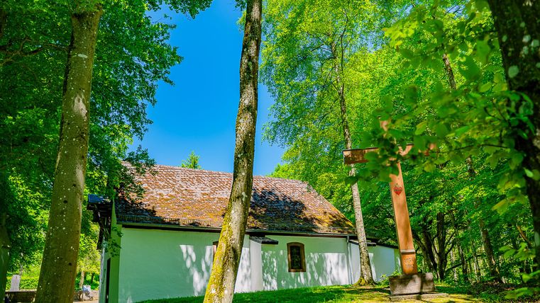 Ein charmantes, kleiner Bau inmitten von grünen Bäumen. Der Himmel ist klar und blau, was eine friedliche Atmosphäre schafft.