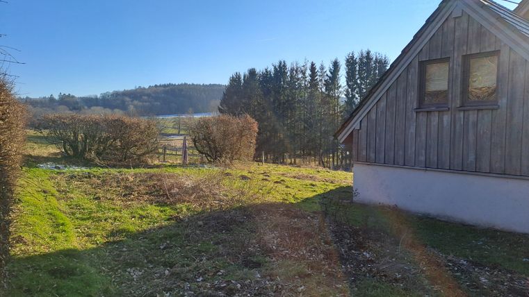Ein gemütliches Holzhaus in einer ländlichen Umgebung. Im Hintergrund sind Bäume und sanfte Hügel sichtbar.