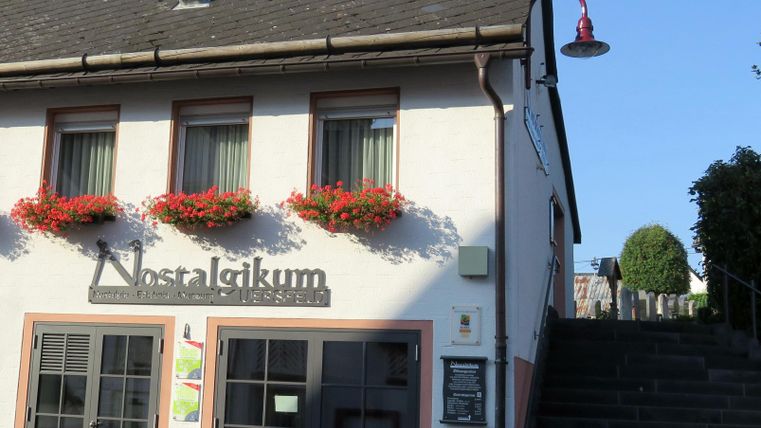 Ein charmantes Gebäude mit dem Namen "Nostalikum" an der Fassade. Blumenkästen schmücken die Fenster und ein Treppenaufgang führt nach oben.