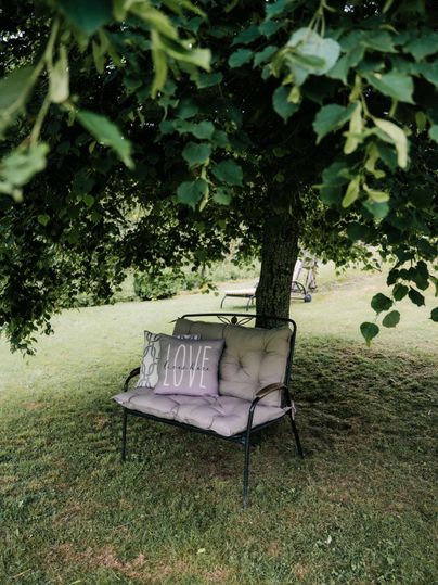 Ein gemütliches Sofa unter einem Baum mit einem Kissen, auf dem „LOVE“ steht. Die Umgebung ist grün und einladend.