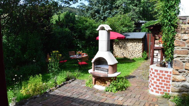 Ein gemütlicher Garten mit einem Grill und Sitzgelegenheiten. Die grüne Umgebung und der sonnige Himmel laden zum Entspannen ein.