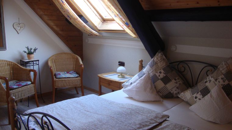 Ein gemütliches Schlafzimmer mit einem Doppelbett und zwei bequemen Sesseln. Die Dachschrägen und das große Fenster sorgen für eine helle und einladende Atmosphäre.