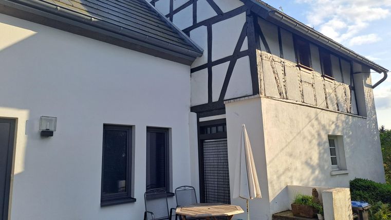 Ein gemütliches Haus mit einem modernen Anbau und traditioneller Fachwerkarchitektur. Auf dem Außenbereich sind ein Tisch und Stühle platziert, umgeben von Pflanzen.
