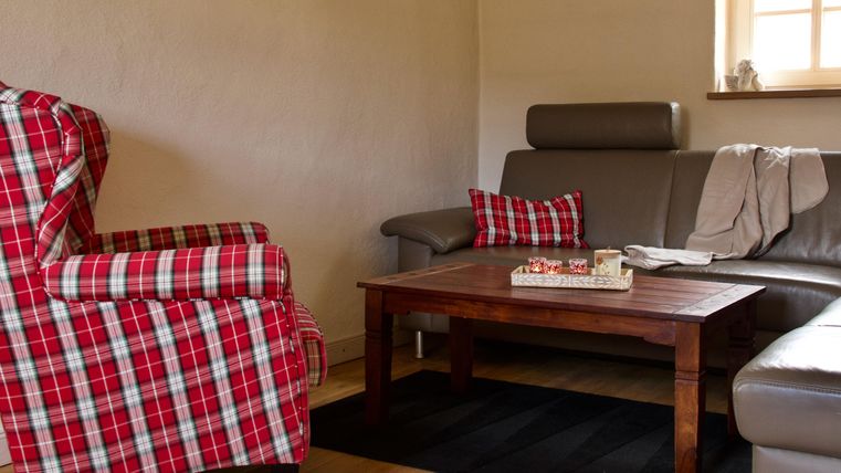 Ein gemütliches Wohnzimmer mit einem karierten Sessel und einer grauen Couch. Auf dem Tisch steht eine Dekoration und ein paar Kerzen.