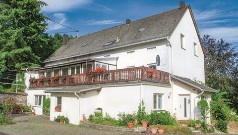Ein schönes, weißes Haus mit einem Balkon und Blumen auf der Terrasse. Es befindet sich in einer grünen Umgebung mit Bäumen.