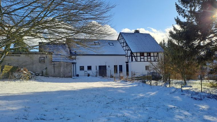 Ein ruhiges Haus im Winter mit schneebedecktem Garten. Der Himmel ist klar und blau, umgeben von Bäumen.