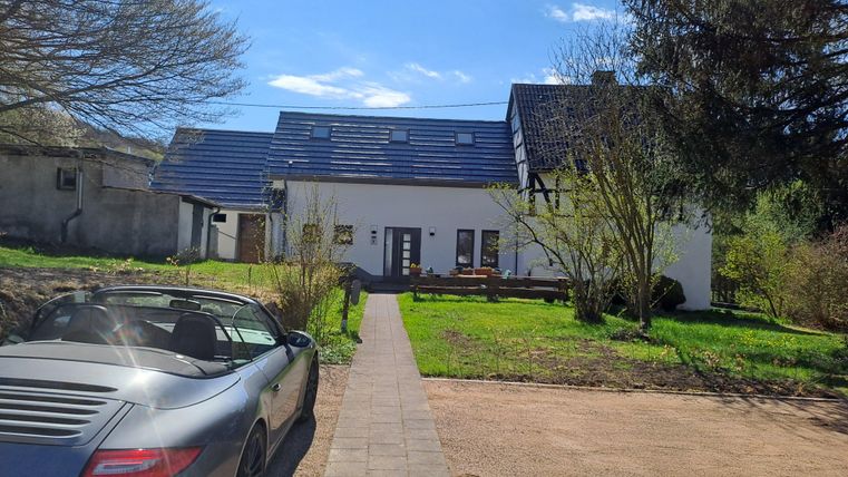 Ein modernes Haus mit einem gepflegten Garten und einem Weg aus Steinen. Im Vordergrund steht ein sportliches Auto.