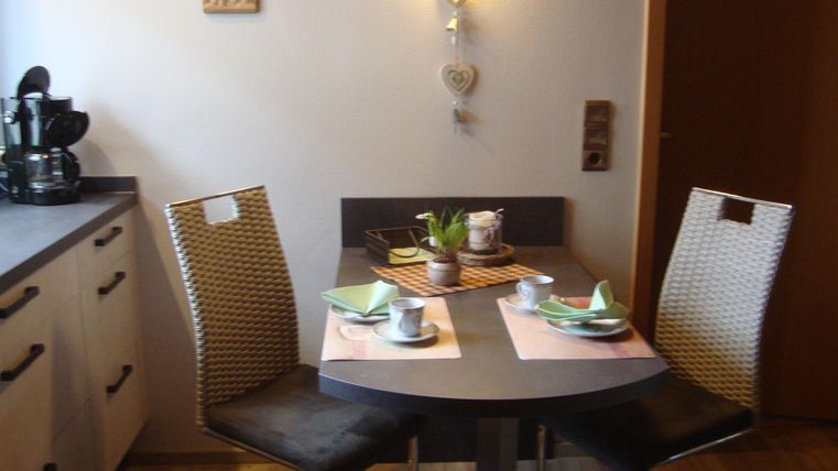 Eine moderne Küchenecke mit einem runden Tisch und zwei Stühlen. Der Tisch ist liebevoll gedeckt mit Geschirr und einem kleinen Blumenarrangement.
