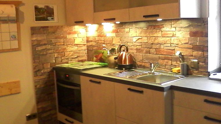 Eine moderne Küche mit Holzschränken und einer Steinwand. Es gibt einen Herd, eine Spüle und eine Edelstahlkanne auf der Arbeitsplatte.