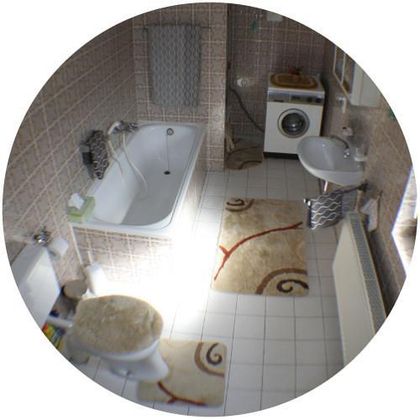 Ein Badezimmer mit einer Badewanne, einem Waschbecken und einer Waschmaschine. Der Raum hat helle Fliesen und einen Teppich mit einem dekorativen Muster.