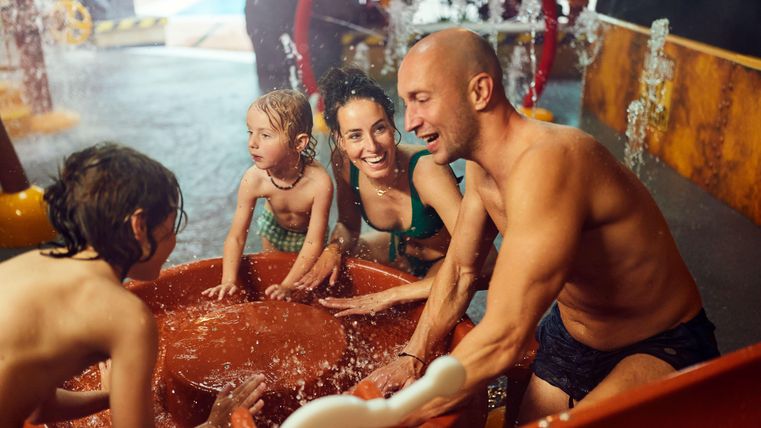 Eine fröhliche Familie spielt im Wasserpark. Kinder und Erwachsene genießen gemeinsam das Wasser und die sprudelnden Fontänen.