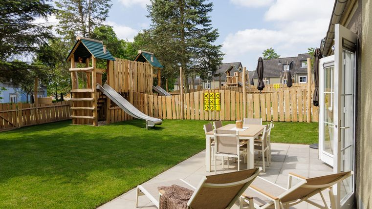 Ein schöner Garten mit einem Spielplatz, der eine Rutsche und ein Spielhaus enthält. Ein Sitzbereich mit Tisch und Stühlen lädt zum Entspannen ein.
