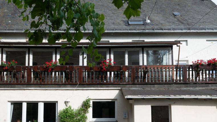Ein modernes Haus mit einem Balkon, der mit bunten Blumen dekoriert ist. Im Vordergrund befinden sich Fenster und eine grüne Pflanze.