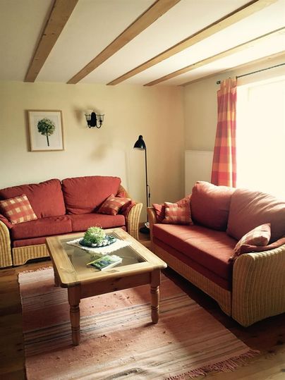 Ein gemütliches Wohnzimmer mit zwei roten Sofas und einem Holztisch. Die Fenster sind mit Vorhängen geschmückt, und ein schönes Bild hängt an der Wand.