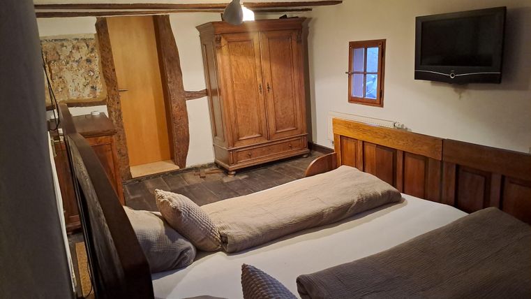 Ein gemütliches Schlafzimmer mit zwei Betten, einem Holzschrank und einem Fernseher. Die Räume haben rustikalen Charme mit sichtbaren Deckenbalken.
