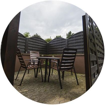 Ein kleiner, gemütlicher Innenhof mit einem Tisch und zwei Stühlen. Die Umgebung ist von einer hohen Holzlattenzaun umgeben.