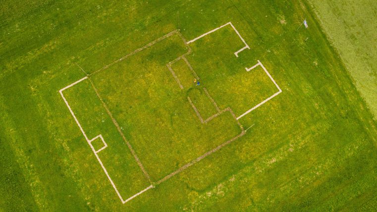Eine grüne Wiese mit den Umrissen eines Gebäudes in Form von weißen Linien. Die Struktur ist teilweise sichtbar und umgeben von frischem Gras.