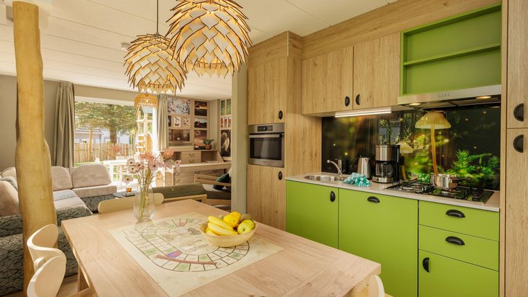 Moderne Küche mit grünen Akzenten und Holzregalen. Ein hölzernes Esstisch mit Obst steht im Vordergrund.