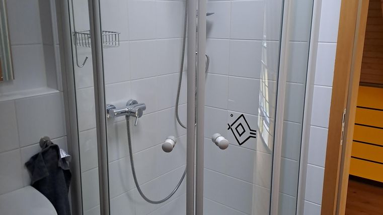 Eine moderne Duschkabine mit gläsernen Türen und einer Handbrause. Die Wände sind mit weißen Fliesen gestaltet.