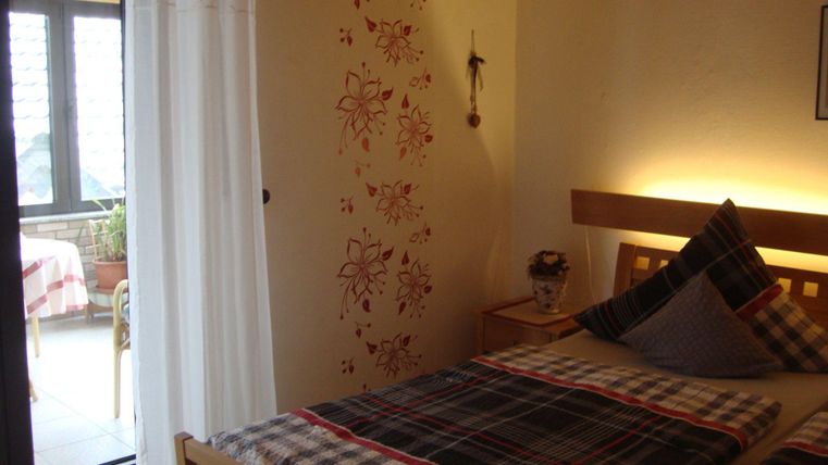 Ein gemütliches Schlafzimmer mit einem Doppelbett und einer Holzbank. Der Raum hat große Fenster und eine helle, einladende Atmosphäre.