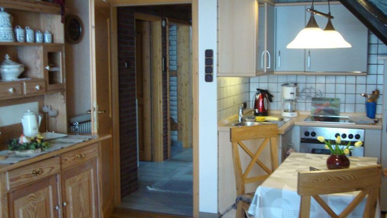 Eine gemütliche Küche mit Holzschränken und einem Esstisch. Die Ausstattung umfasst einen Herd, eine Kaffeemaschine und einen Kühlschrank.